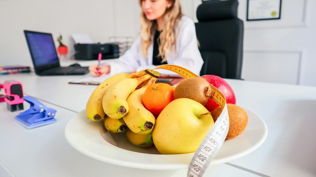 a woman sitting at a desk with a bowl of fruit